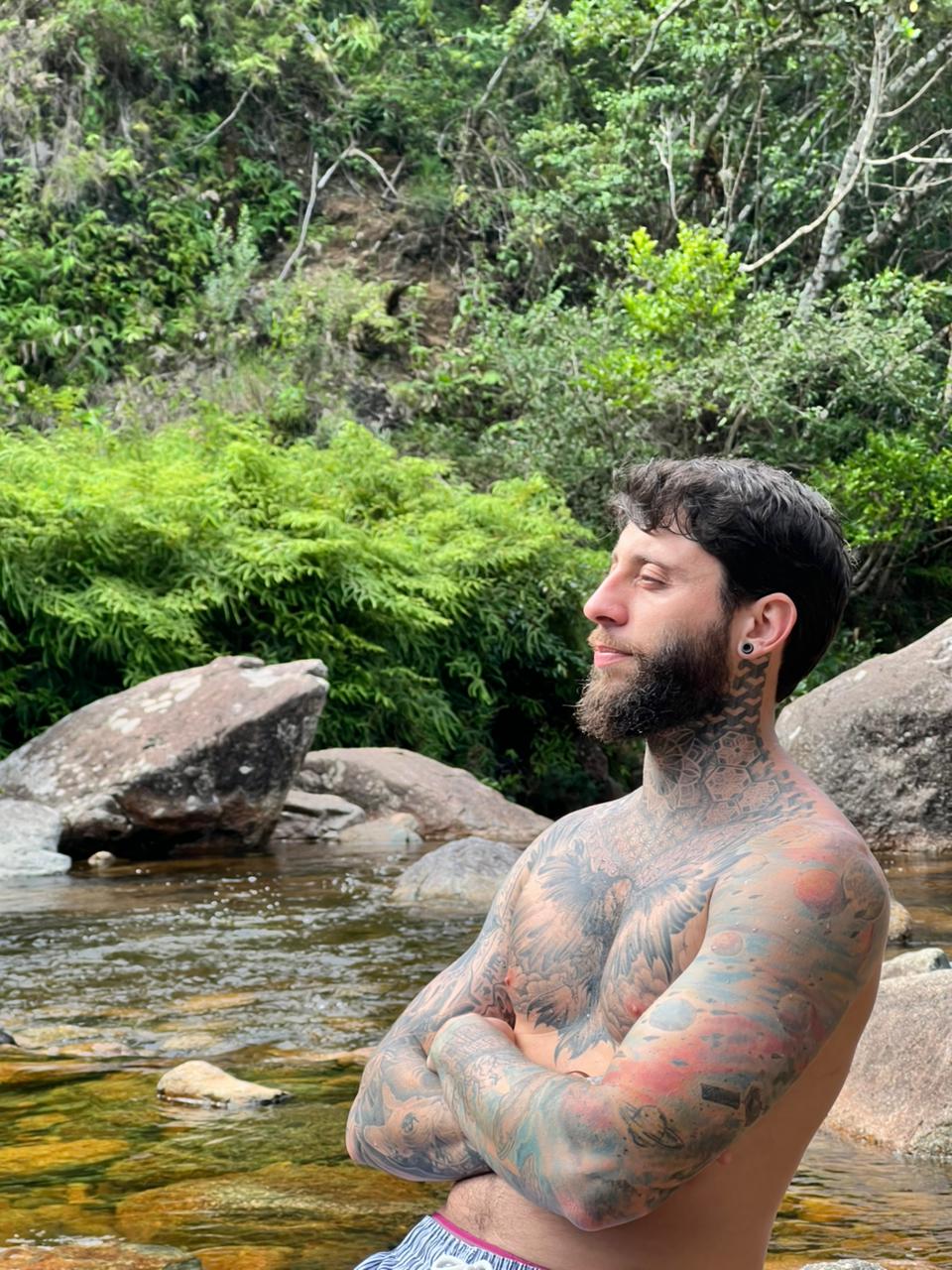 Homem em contemplação junto a um rio cercado por mata